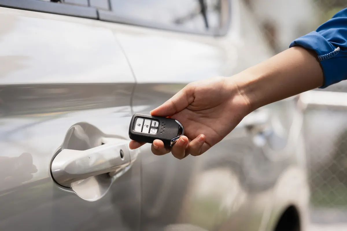 Main tenant une clé mains libres près de la poignée d’une voiture grise