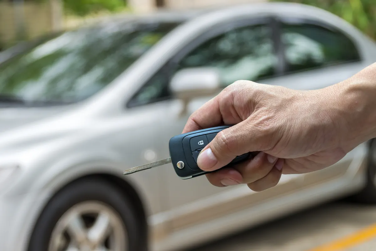 Main pointant une clé pliante à télécommande vers une voiture grise