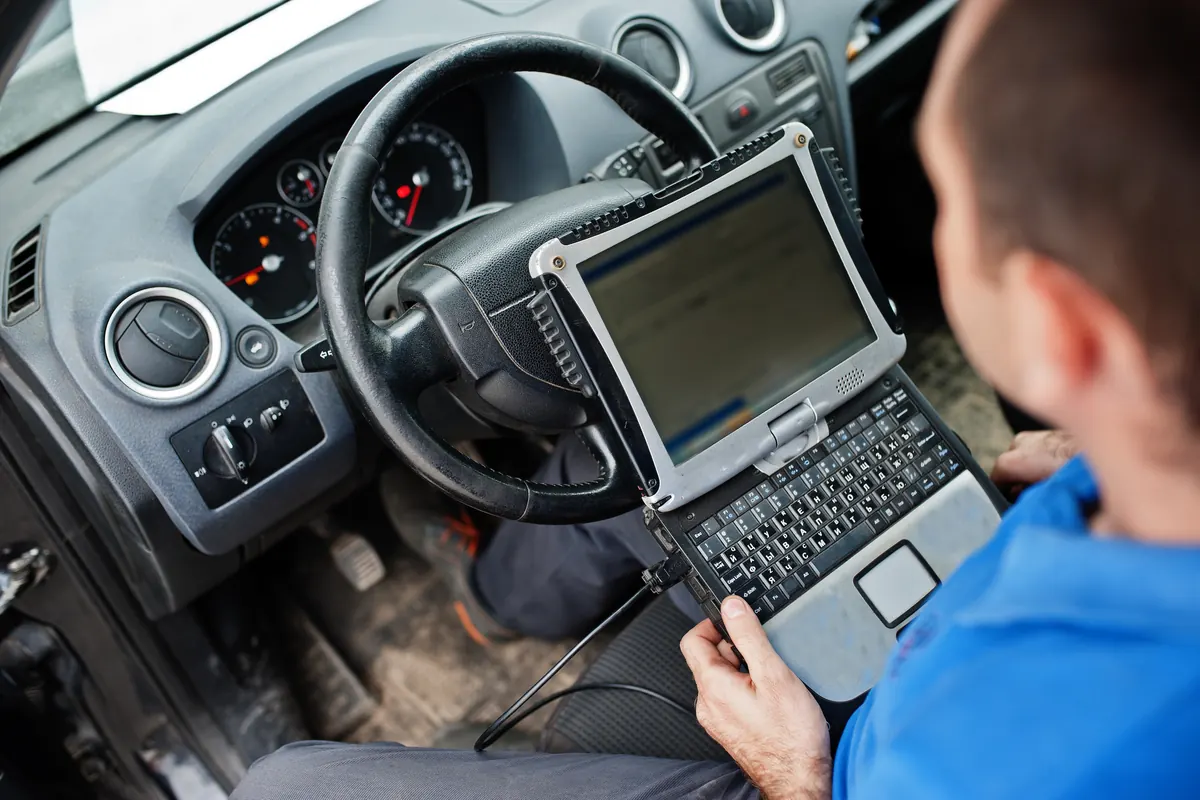 Technicien au volant, ordinateur de diagnostic relié à la voiture