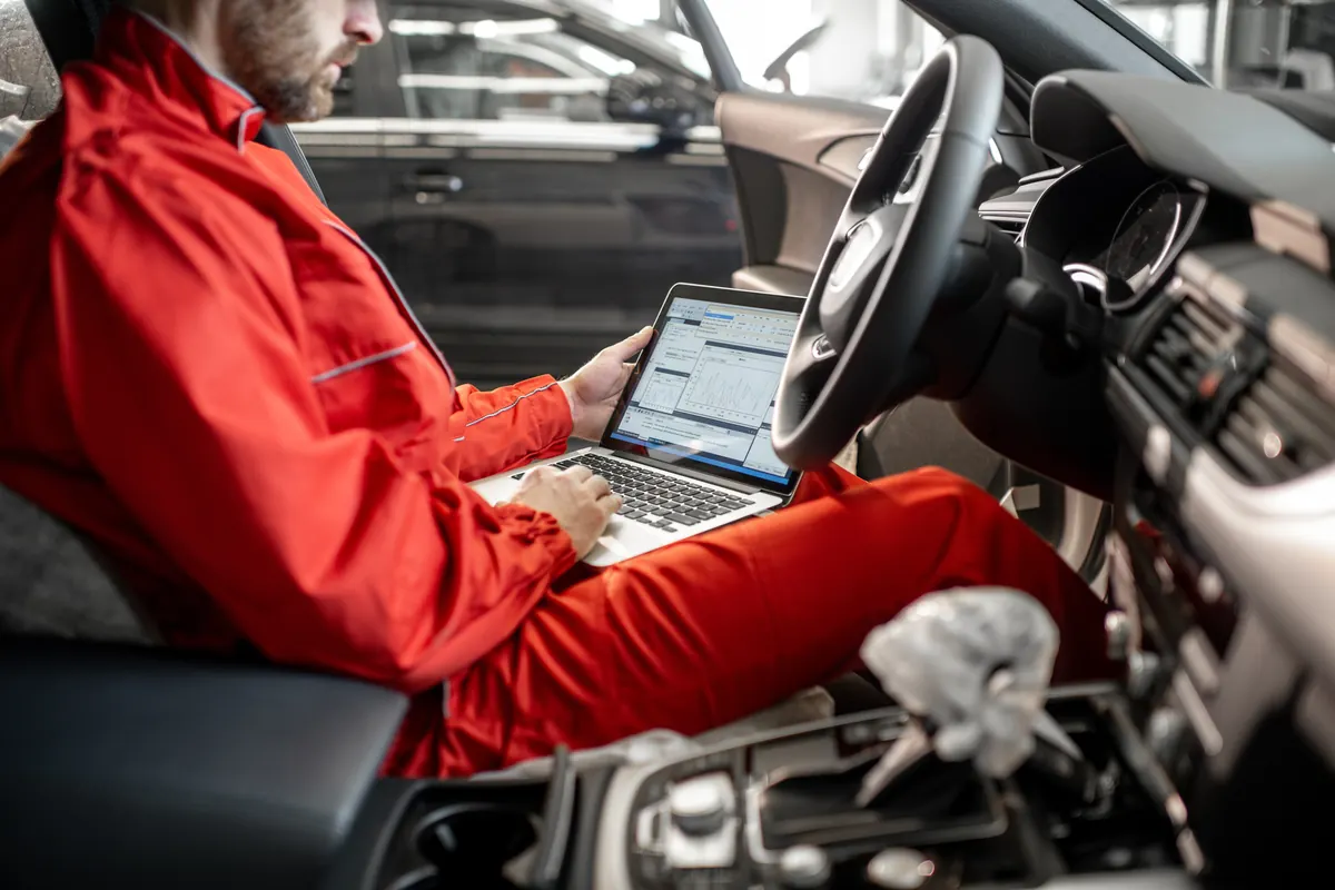 Technicien assis au volant, ordinateur portable relié à la voiture
